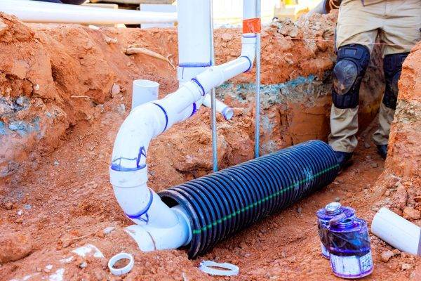 Worker are busy placing black drainage pipe among newly laid white PVC in trench at construction site